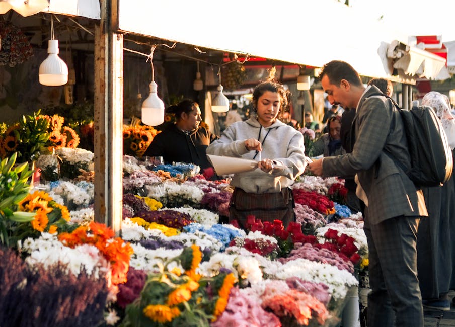 A vibrant outdoor flower market scene featuring a floral arrangement vendor showcasing a wide array of fresh flowers, including sunflowers, chrysanthemums, roses, and asters in various colors such as 