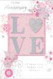 This anniversary card presents a gentle celebration of enduring romance, its design built around soft pastel pinks, silvery greys, and pearlescent whites that evoke the muted elegance of an English spring morning in Enfield. At the centre, the word "LOVE" stands out in raised, softly rounded letters, completely coated in a fine layer of glitter. The letter "O" is imaginatively replaced by a shimmering silver heart, slightly more textured than the surrounding letters, giving a distinct point of tactile interest. The glitter finish glows rather than glares, adding sophistication to the otherwise tender palette. Around this central motif, delicate illustrated blooms in blush and mauve unfurl across the card with a watercolour softness, their outlines refined and their shading subtle. Slender vines and graceful swirls link the flowers together, creating a flowing framework that guides the eye from top to bottom, much like the way a florist in Enfield would guide the line of a romantic bouquet. Tiny decorative touches-scattered petals, small curls, and faint butterflies-add hints of motion and whimsy, as if a gentle breeze were blowing through a garden near Enfield Town. The background remains a pale, warm pink, allowing the silver accents and floral details to stand out clearly without crowding the space. The phrases "On Our Anniversary" and "I love you today and always" are written in an elegant, understated script, providing a heartfelt message that matches the soft, intimate feel of the artwork. Overall, the card looks like a keepsake designed to mark a shared journey with quiet grace and deep affection.